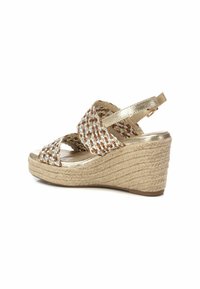 Sandalia de cuña con parte superior de tejido trenzado en tonos dorados y marrones, detalles metálicos y base con textura de yute para mayor agarre y estilo.