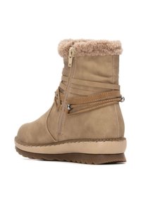 Botín de tobillo marrón con cuello de piel sintética, cremallera lateral y correas superpuestas. Punta redondeada y suela de goma texturizada con un ligero agarre.