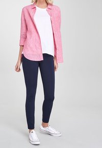 Lichtroze linnen overhemd met knopen over een wit T-shirt, gecombineerd met marineblauwe leggings en witte sneakers. Gladde stof en een aangesloten ontwerp.