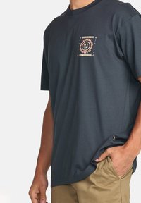 T-shirt en coton bleu marine à col rond, avec un design graphique central en orange et blanc. Manches courtes, coupe décontractée.