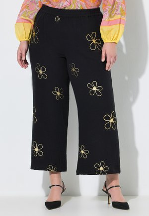 Černé kalhoty s širokými nohavicemi s vyšívanými zlatými květinami, nošené s černými lodičkami na jehlovém podpatku a barevnou dlouhými rukávy.