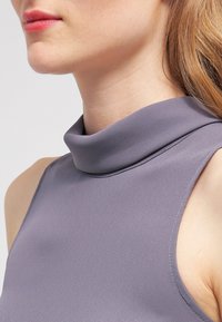 Top senza maniche con colletto alto in morbido tessuto grigio. Presenta una texture liscia e cuciture sottili lungo il collo, progettato per una vestibilità aderente.