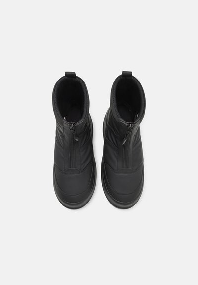 Bottes de cheville noires imperméables avec un extérieur en cuir lisse, des zippers à l'avant et un intérieur doublé en polaire pour le confort.