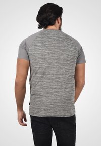 Camiseta gris de manga corta con un patrón texturizado, con mangas raglán en un gris más claro. Fabricada en material suave, de corte informal.
