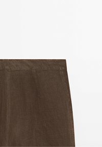 Pantalons en lin marron présentant une surface texturée, une taille plate et une coupe droite. Le tissu a un éclat subtil et une finition structurée.