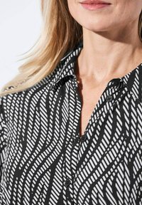 Zwart-wit blouse met een golvende gestreepte patroon, knoopsluiting aan de voorkant en kraagdetails. Zachte stof met een gladde textuur.