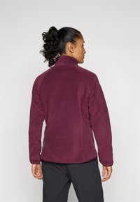Giacca in pile di un profondo bordeaux con colletto alto, caratterizzata da una texture liscia e un design aderente, mostrata da dietro.