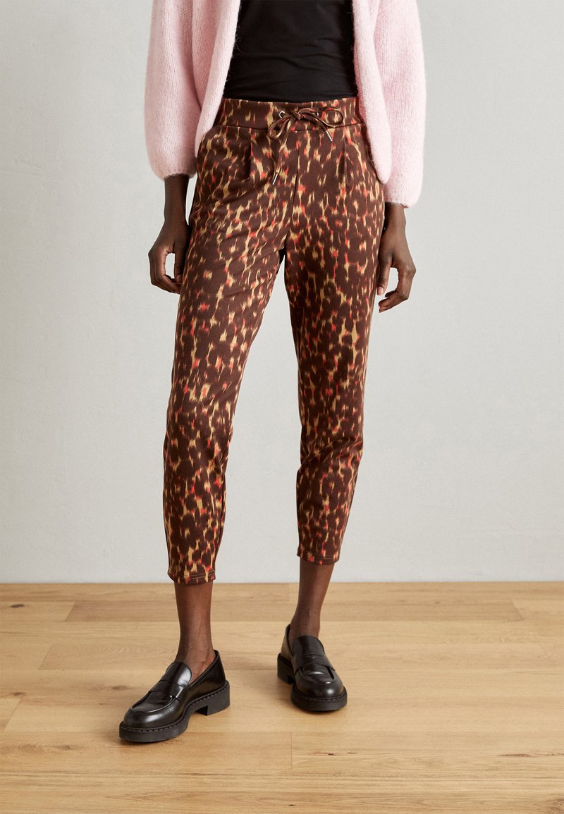 Pantaloni scurți maro cu un model de leopard multicolor, având talie cu șnur și buzunare laterale, asortați cu pantofi loafers negri.