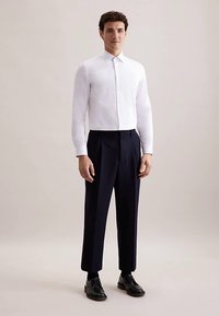 Witte lange mouwen blouse met een button-down kraag, gecombineerd met marineblauwe broek met een getailleerde pasvorm en zwarte leren schoenen.