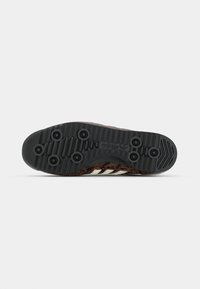 Suola delle scarpe Adidas in gomma nera con caratteristiche di trazione prominenti. La parte superiore ha un motivo in pelle di serpente marrone e beige. Tre strisce bianche in evidenza.