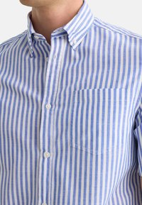 Camisa de botones a rayas azul y blanca con cuello, mangas cortas y un bolsillo en el pecho. Fabricada con un tejido ligero y de textura suave.