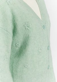 Cardigan lavorato a maglia verde menta con scollo a V, cinque bottoni e dettagli in ricamo floreale. Texture morbida con accenti a coste sui bordi.