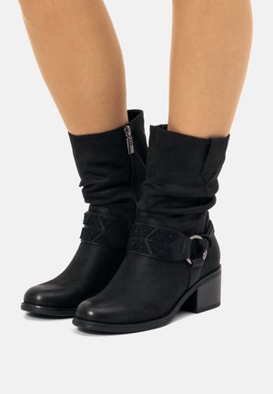 Schwarze Knöchelboots mit einem lässigen Design, ausgestattet mit einem seitlichen Reißverschluss, einem strukturierten Riemen mit geometrischen Mustern und einem flachen Blockabsatz.