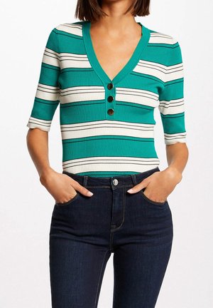 Groen-wit gestreept geribd topje met een V-halslijn en drie knopen, gecombineerd met donkerblauwe hoge taille jeans.