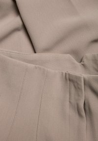 Beige kangas, jolla on sileä pinta, jossa on hienovaraisia viivoja ja ommeltuja saumoja, järjestetty päällekkäin osissa.