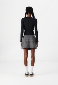 Zwarte langemouwtop, aansluitende pasvorm. Geruite mini-jurk in zwart en wit. Witte enkelkousen met zwarte sneakers. Eenvoudige, casual outfit.