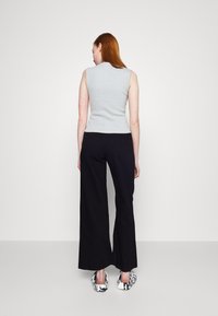 Gray sleeveless top with a high neckline paired with wide-leg black trousers. Footwear features a black and white abstract pattern.
