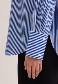 Camicia a righe blu e bianche con polsini bottonati, caratterizzata da maniche lunghe e orlo dritto, realizzata in un tessuto liscio.