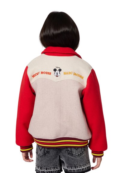 Bambino che indossa una giacca rossa e beige di Mickey Mouse x Marc Jacobs con polsini e orlo a righe, abbinata a pantaloncini in denim neri, visto di spalle.