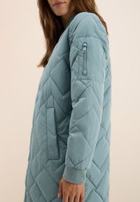 Giacca a vento trapuntata di un blu chiaro, con motivo a zigzag, tasche laterali, polsini a coste e una tasca con zip sul braccio.
