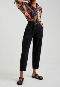 Bloemmotief, doorzichtige blouse met korte mouwen en trekkoord, gecombineerd met hoge, losse zwarte broeken en platte zwarte sandalen.