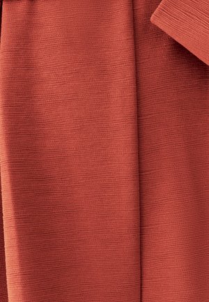 Close-up van opgevouwen textiel met een warme terracottakleur en zichtbare horizontale ribbels.