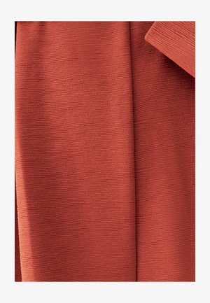 Detailní záběr složené texturované látky v teplé terakotové barvě s viditelnými vodorovnými hřebeny.