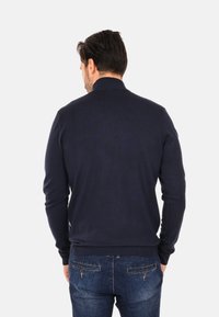 Maglione a maglia blu navy con collo alto, motivo strutturato e polsini e orlo a coste. Indossato con jeans di denim blu.