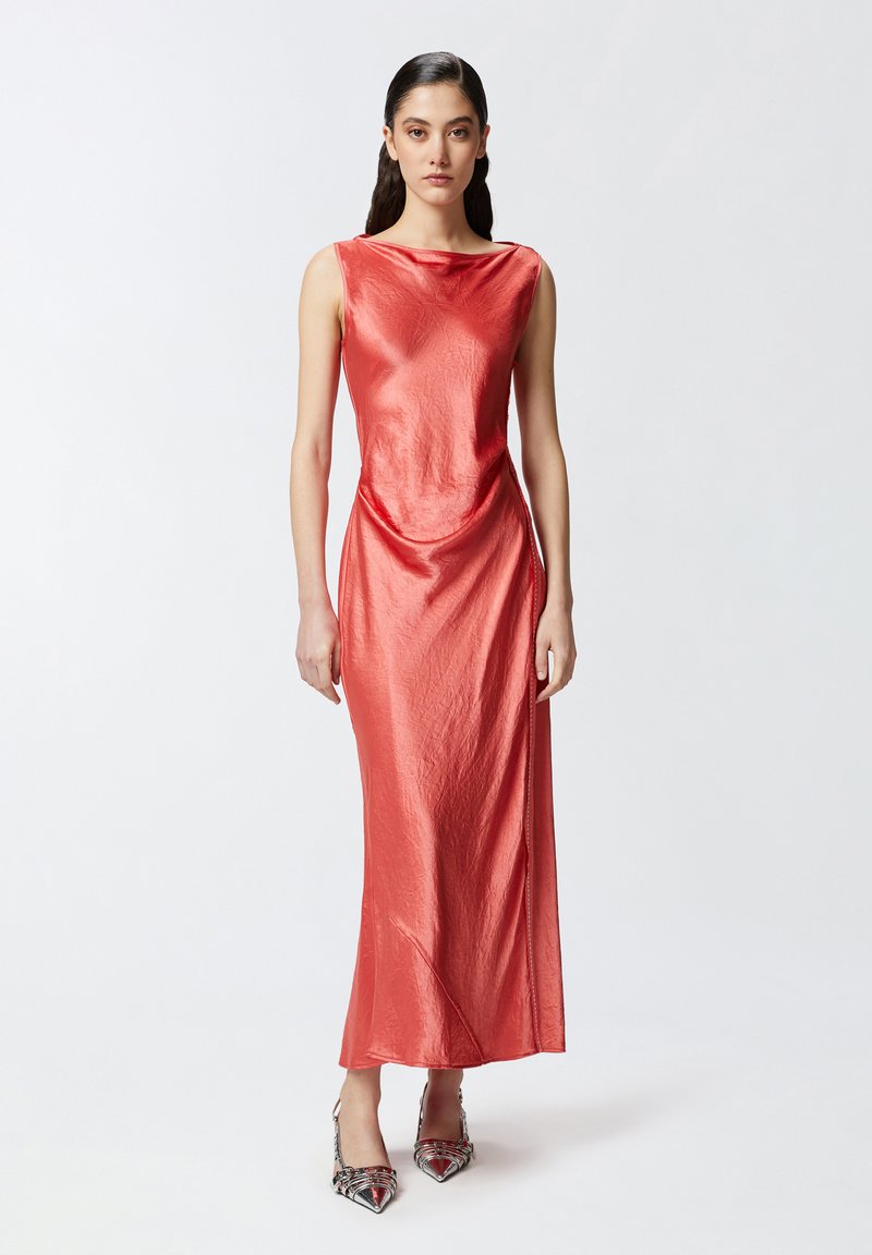 Duga, bezrukava, uska haljina u svijetloj koraljno-crvenoj boji s glatkom, sjajnom teksturom i drapiranim detaljem u struku. Uparena sa cipelama s uzorkom.