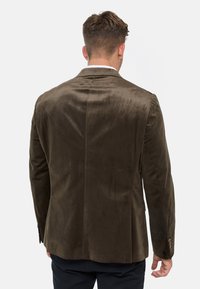 Brun fløyelsblazer med slim fit, spiss krage og detaljert søm. Glatt tekstur med fire knapper på hver erme.