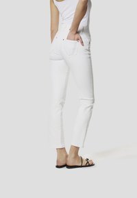 Bílé džínové kalhoty s přiléhavým střihem, opatřené zadními kapsami a jemnou výšivkou u spodního lemu. Nošeny s černými plochými sandály.