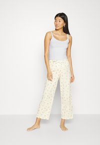 Top in morbido viola chiaro con pizzo, abbinato a pantaloni da pigiama larghi in crema con motivo floreale, vita elastica e dettaglio con lacci.