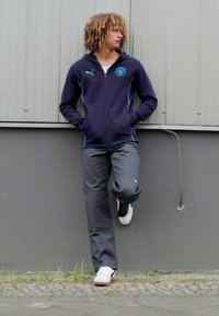 Námorná športová bunda so zipsom a svetlomodrými akcentmi, šedé nohavice a biele tenisky. Vystužené logo Puma na bunde a nohaviciach.
