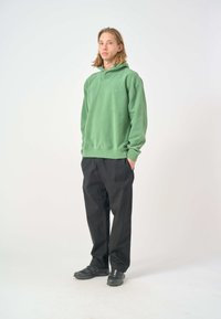 Green hoodie made of soft fabric with a relaxed fit, paired with loose black pants and black shoes. Simple design, minimal branding.