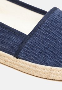 Navy canvas espadrille featuring a textured upper and a jute rope sole, with a smooth lining and reinforced stitching along the edges.