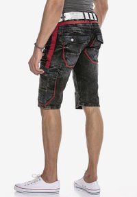 Zwarte denim cargoshorts met rode accenten, meerdere zakken en een gestructureerde afwerking. Gecombineerd met een witte riem en canvas schoenen.