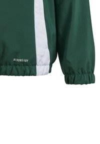 Grüne Jacke mit weißen seitlichen Streifen, aus glattem Material gefertigt. Verfügt über elastische Bündchen und Säume, mit "AEROREADY"-Logo auf der unteren Vorderseite.