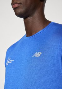 Zils sporta krekls ar teksturētu apdari, ar atstarotāju New Balance logotipu uz krūšu un ar apaļo kakla izgriezumu.