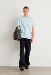 Tricou cu mânecă scurtă de un albastru deschis, pantaloni negri evazați și pantofi negri. Ține o geantă mare gri cu o textură moale, design minimalist.