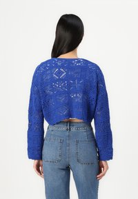 Cropped blue knit sweater with a textured, patterned design and long sleeves, paired with high-waisted denim jeans featuring studded accents.