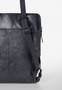 Navy leren schoudertas met verstelbare schouderband, voorzien van een ritsvak en een gladde textuur, verfraaid met stikseldetails.