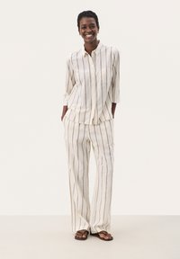 Linned to-delt outfit med en knapp-down skjorte og vide bukser med vertikale striber i crème og brun. Inkluderer en brystlomme.