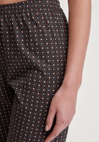 Bruine broek met een geometrisch patroon van diamanten en vierkanten in roze en groen. Elastische tailleband met een gladde, lichte stof.