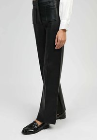 Pantalons en simili cuir noir à coupe droite, dotés de deux poches plaquées à l'avant et de fentes latérales. Associés à des mocassins noirs brillants.