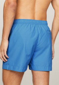 Pantaloni da bagno blu con una vita elastica, texture liscia e una tasca posteriore con un piccolo dettaglio. Tessuto traspirante con una vestibilità comoda.
