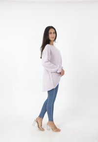 Licht lavendelkleurige oversized trui met verlaagde schouders, gecombineerd met blauwe skinny jeans en doorzichtige hakken. Eenvoudige, ontspannen pasvorm.