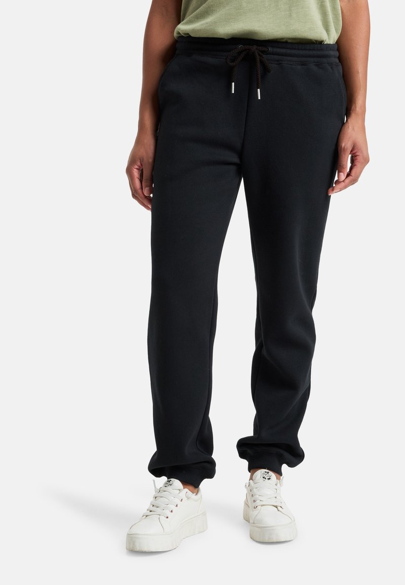 Zwarte sweatpants met een trekkoord in de taille, smal toelopende enkels en zijzakken. Gecombineerd met witte sneakers. Gladde textuur.