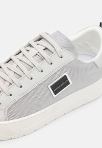Baskets grises avec un dessus texturé, semelle en caoutchouc et lacets bien visibles. Présentent un accent étiqueté noir sur le côté.