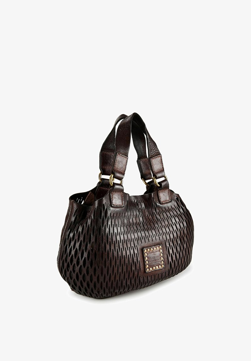 Donkerbruine leren handtas met een textuur van uitgesneden patronen, dubbele handvatten met gouden ringen en een vierkante met studs versierde merkpatch aan de voorkant.