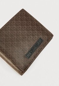 Καφέ πορτοφόλι με υφή, που διαθέτει γεωμετρικό μοτίβο, μαύρο λογότυπο και τετράγωνο σχέδιο με ραμμένες άκρες.